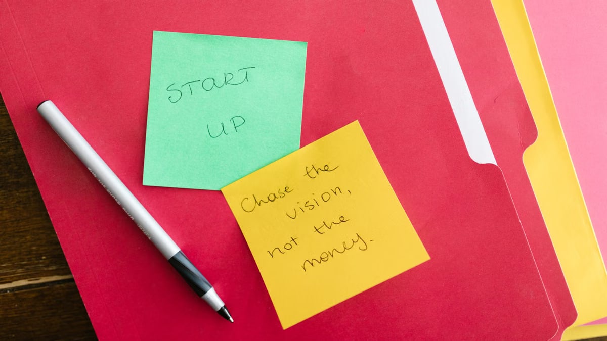 Inspiring startup quotes written on sticky notes placed on colorful folders with a pen.